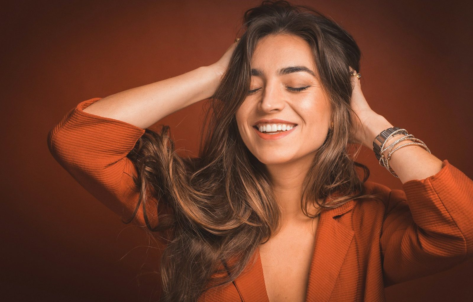 smiling woman in brown top holding hairs