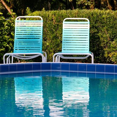 Een ligbed met een dik buitenkussen naast een zwembad op een zonnig terras